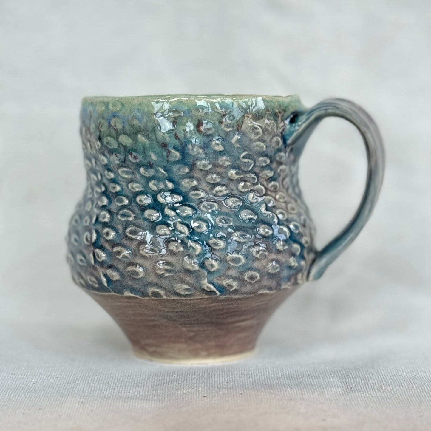 Handmade ceramic mug with textured surface on a light gray background