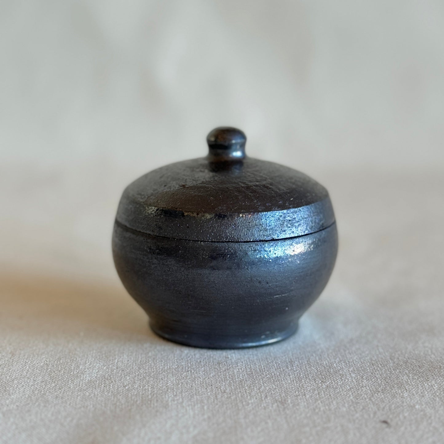 Black ceramic container with lid on a beige background
