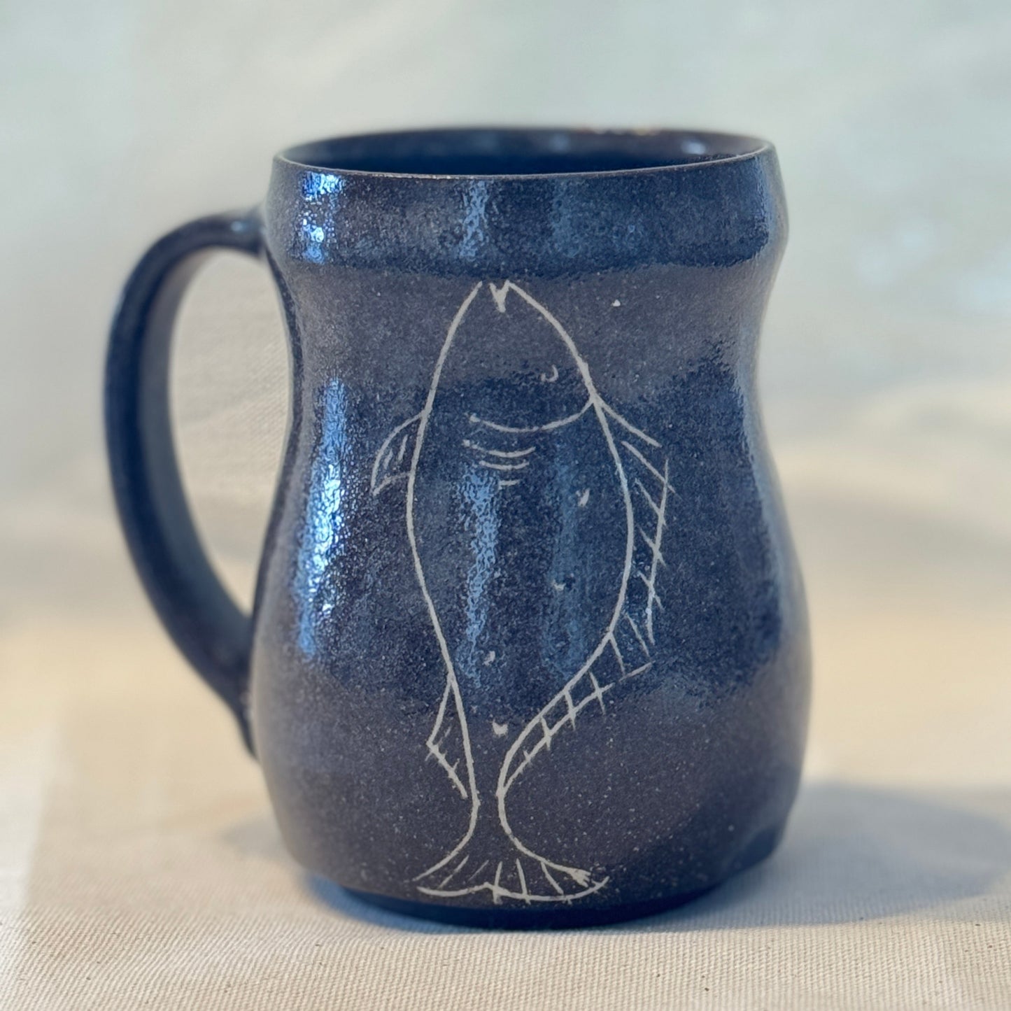 Blue ceramic mug with fish design on a beige surface