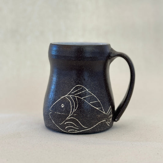 Black ceramic mug with fish design on a light background