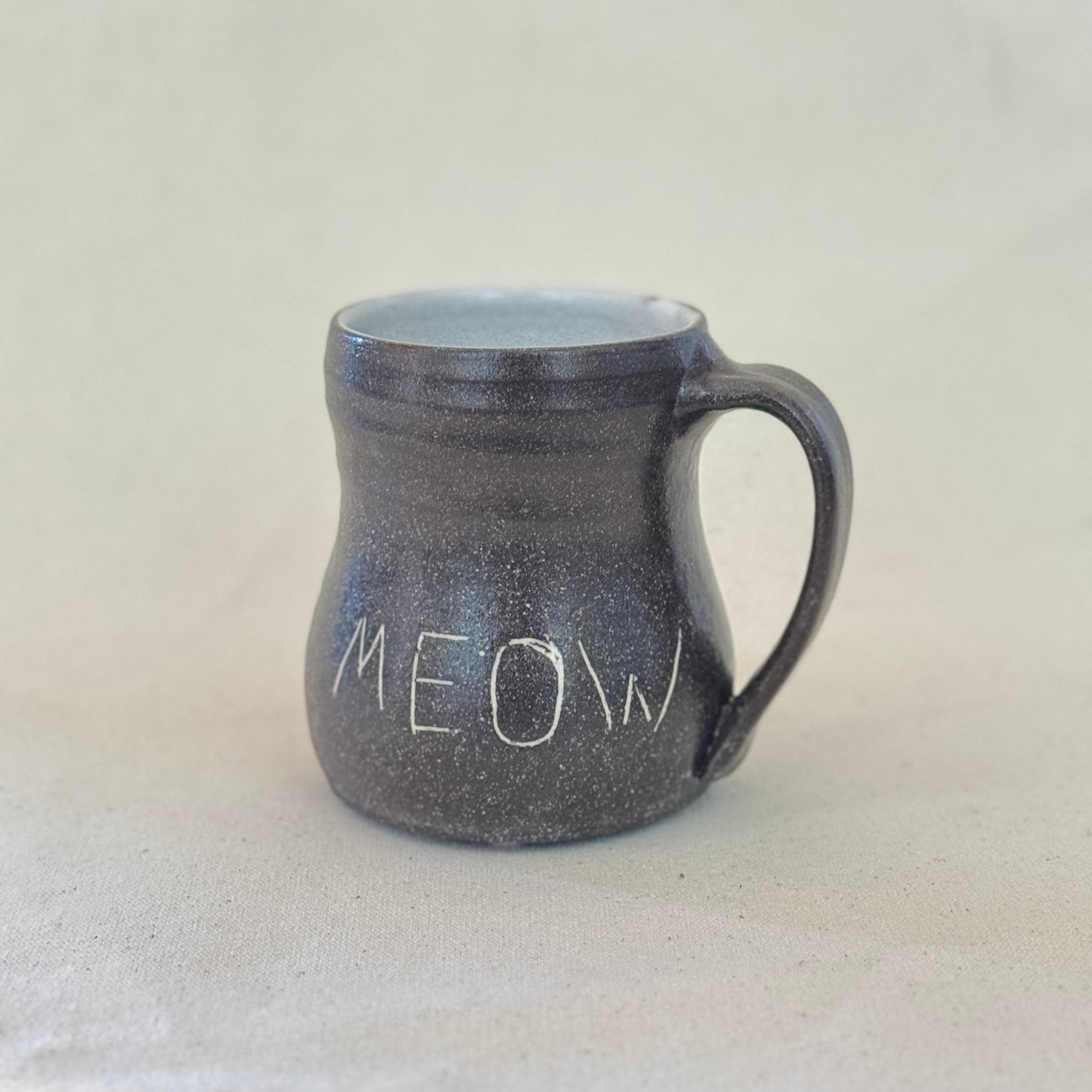 Black speckled mug with 'MEOW' text on a light gray background