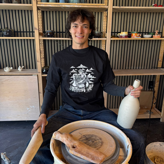 Dax modeling the head in the clouds tee, holding a ceramic bottle in the pot shed