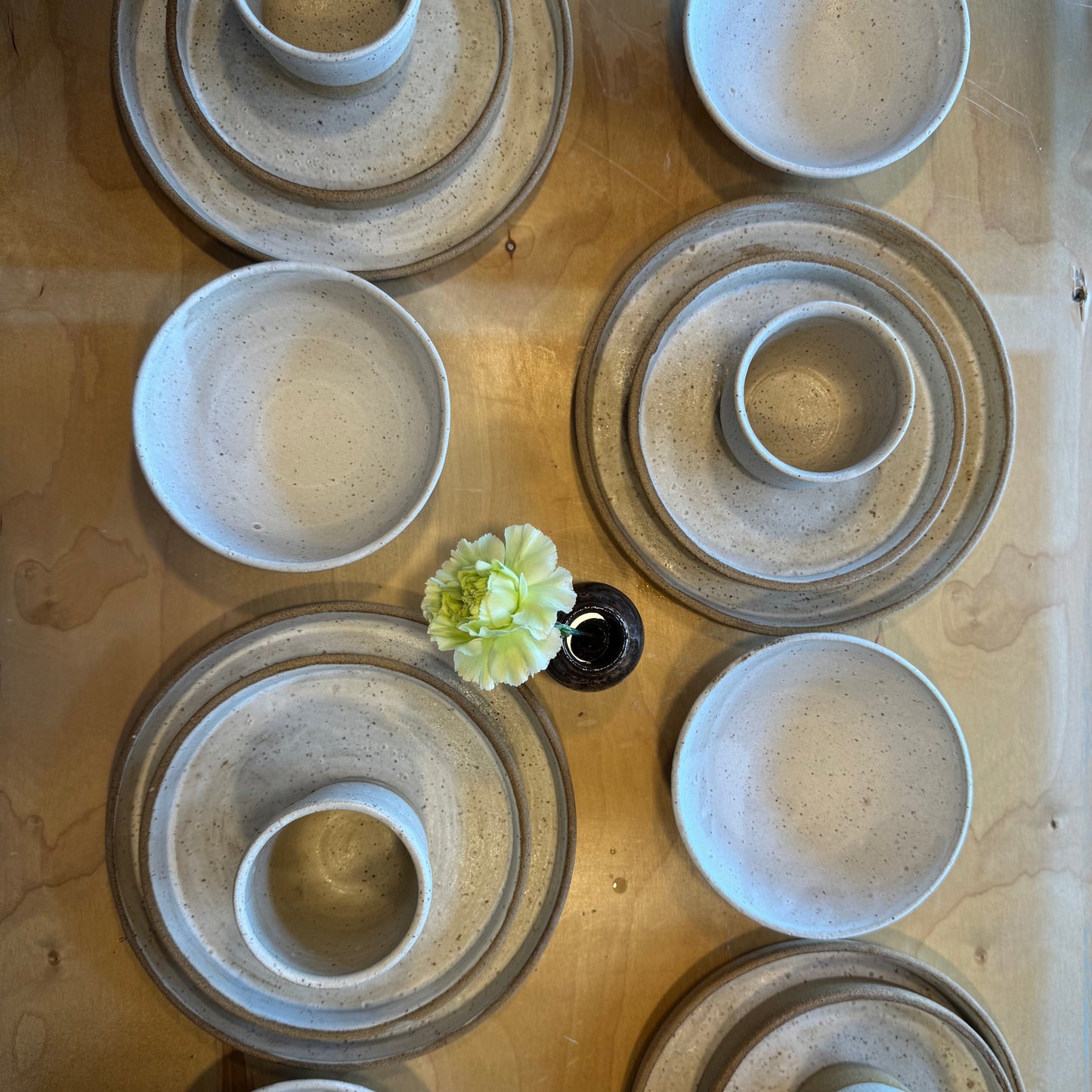 Set of ceramic bowls and plates on a wooden surface with a small green flower.