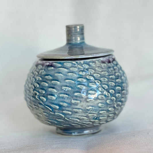Ceramic jar with textured surface and lid on a light fabric background