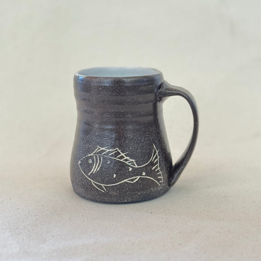 Black ceramic mug with fish design on a light gray background