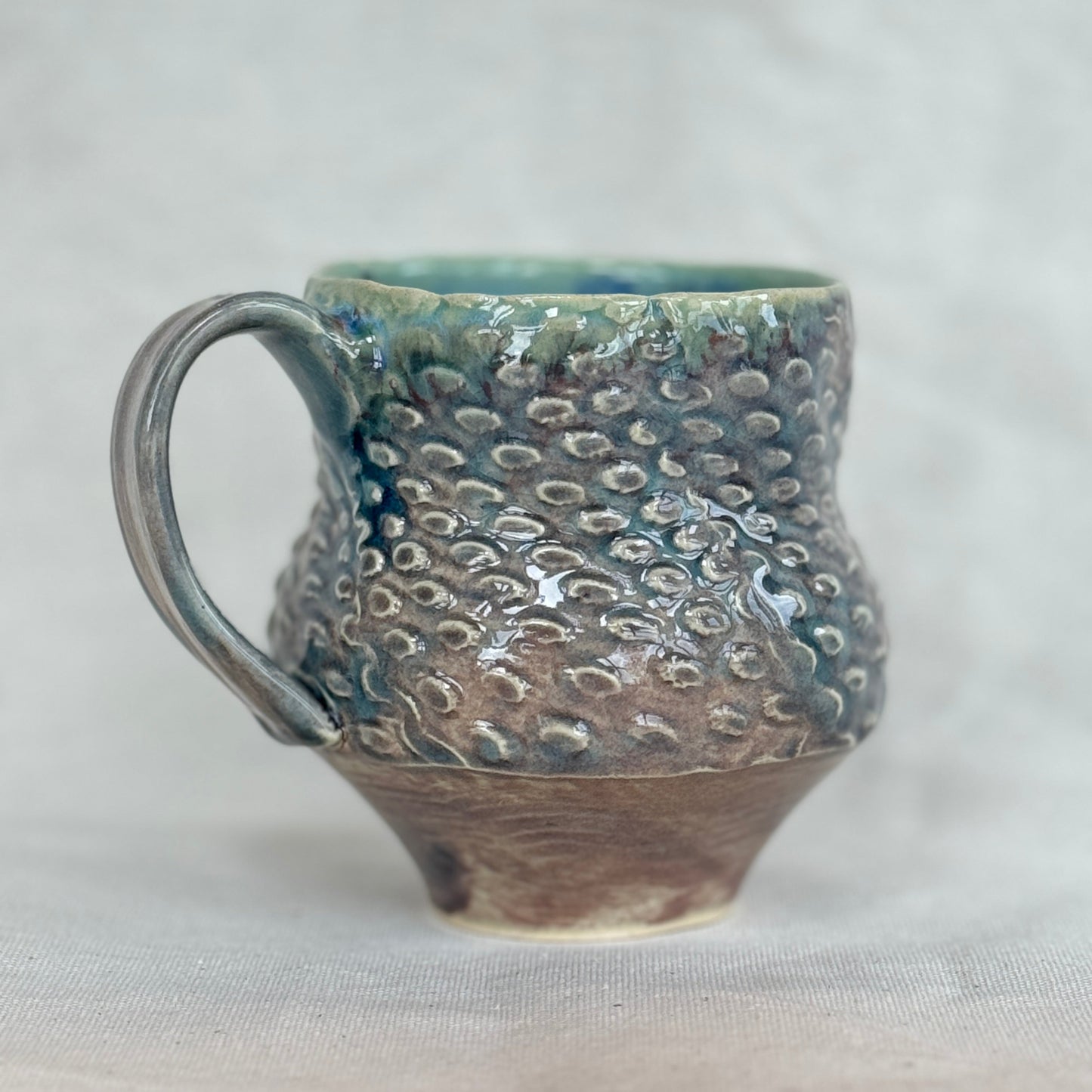 Handmade ceramic mug with textured surface on a light gray background