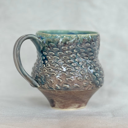 Handmade ceramic mug with textured surface on a light gray background
