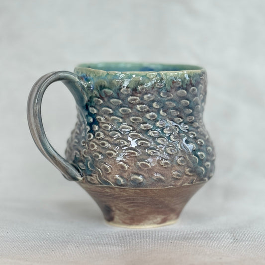 Handmade ceramic mug with textured surface on a light gray background