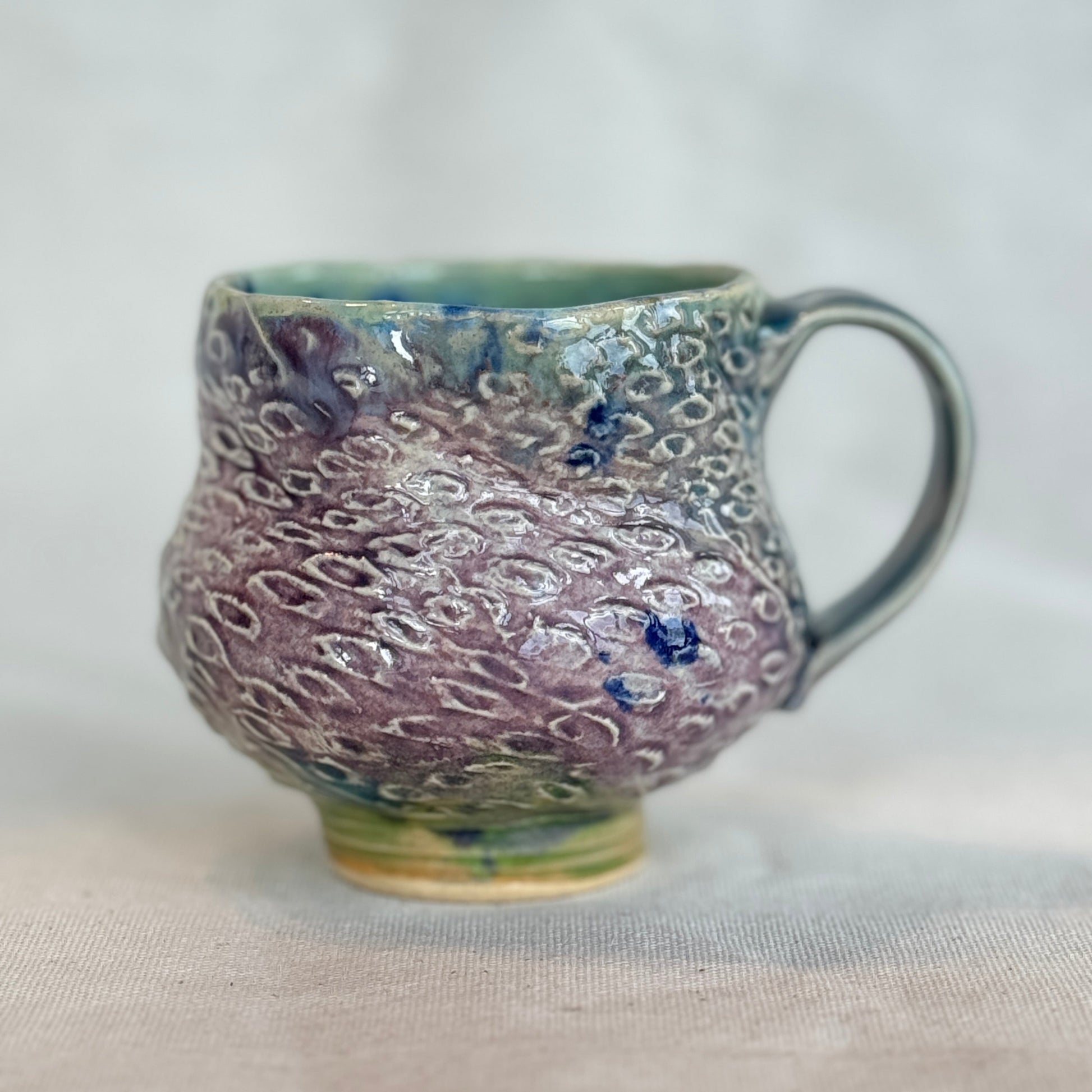 Handmade ceramic mug with textured surface on a light fabric background