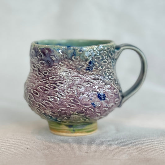 Handmade ceramic mug with textured surface on a light fabric background