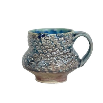 Handmade ceramic mug with textured surface on a light background