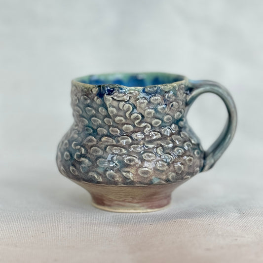 Handmade ceramic mug with textured surface on a light background