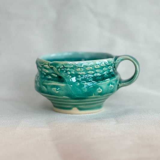 Green ceramic cup with textured surface on a white background