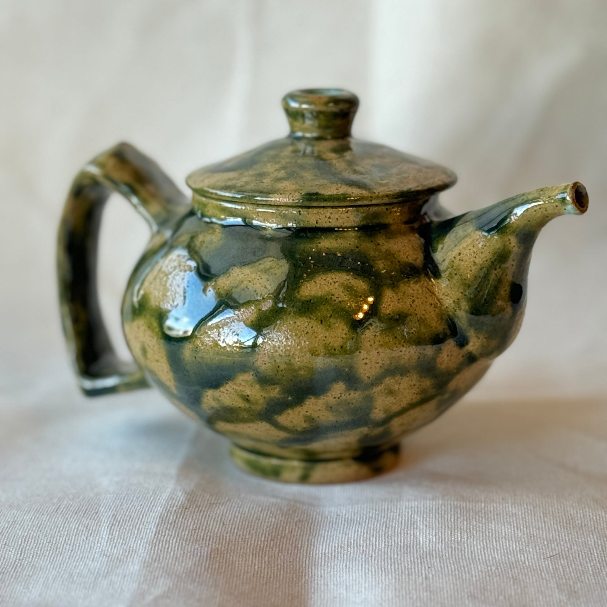 Green ceramic teapot on a white fabric background