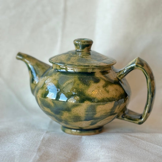 Green ceramic teapot on a white fabric background