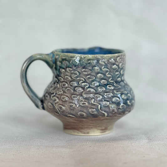 Handmade ceramic mug with textured surface on a light gray background
