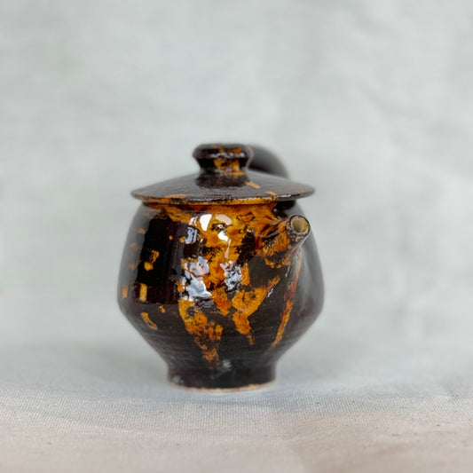 Small ceramic jar with brown and orange glaze on a light gray background