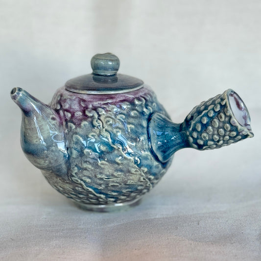 Ceramic teapot with textured surface and purple accents on a white background