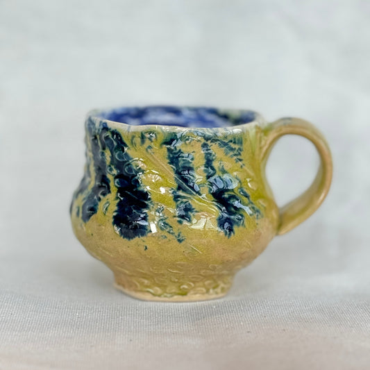 Handmade ceramic mug with blue and green glaze on a white background