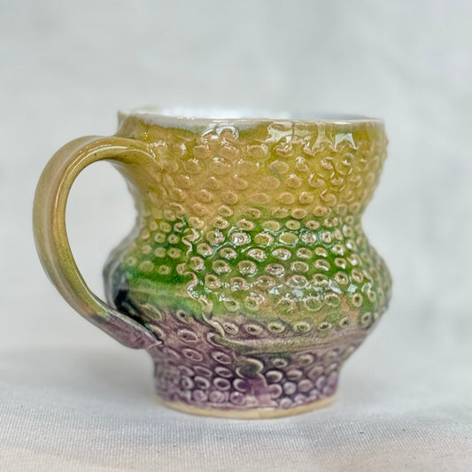 Ceramic mug with textured green and purple design on a white background