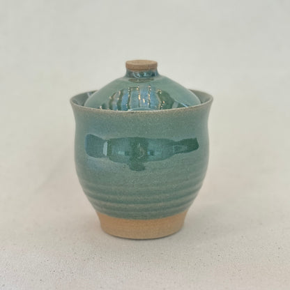 Green ceramic jar with a lid on a light gray background