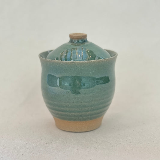 Green ceramic jar with a lid on a light gray background