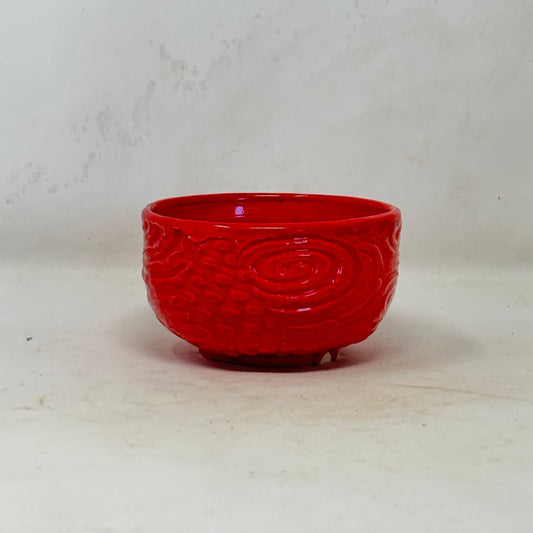 Red ceramic bowl with intricate patterns on a white background
