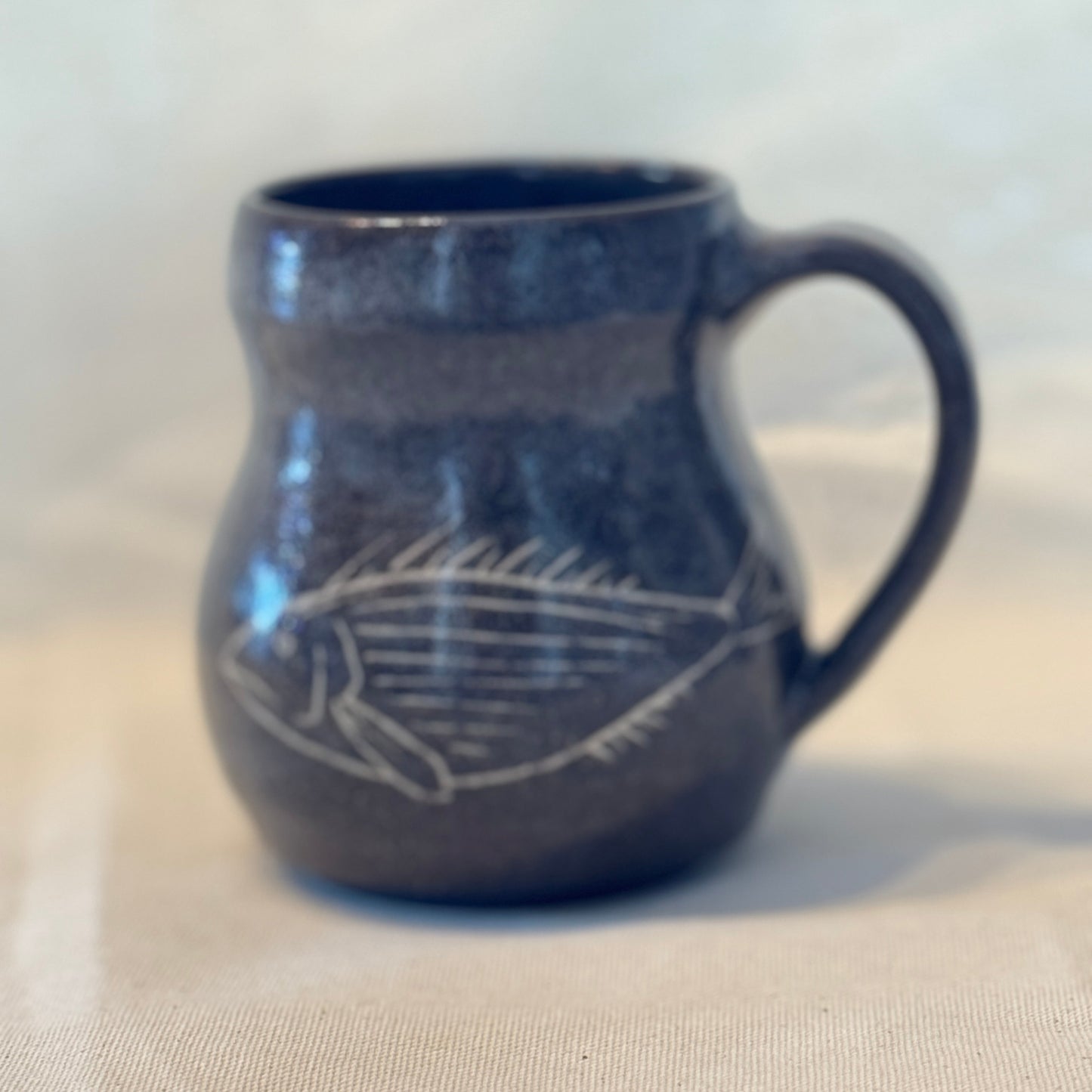Blue ceramic mug with a white fish design on a beige surface