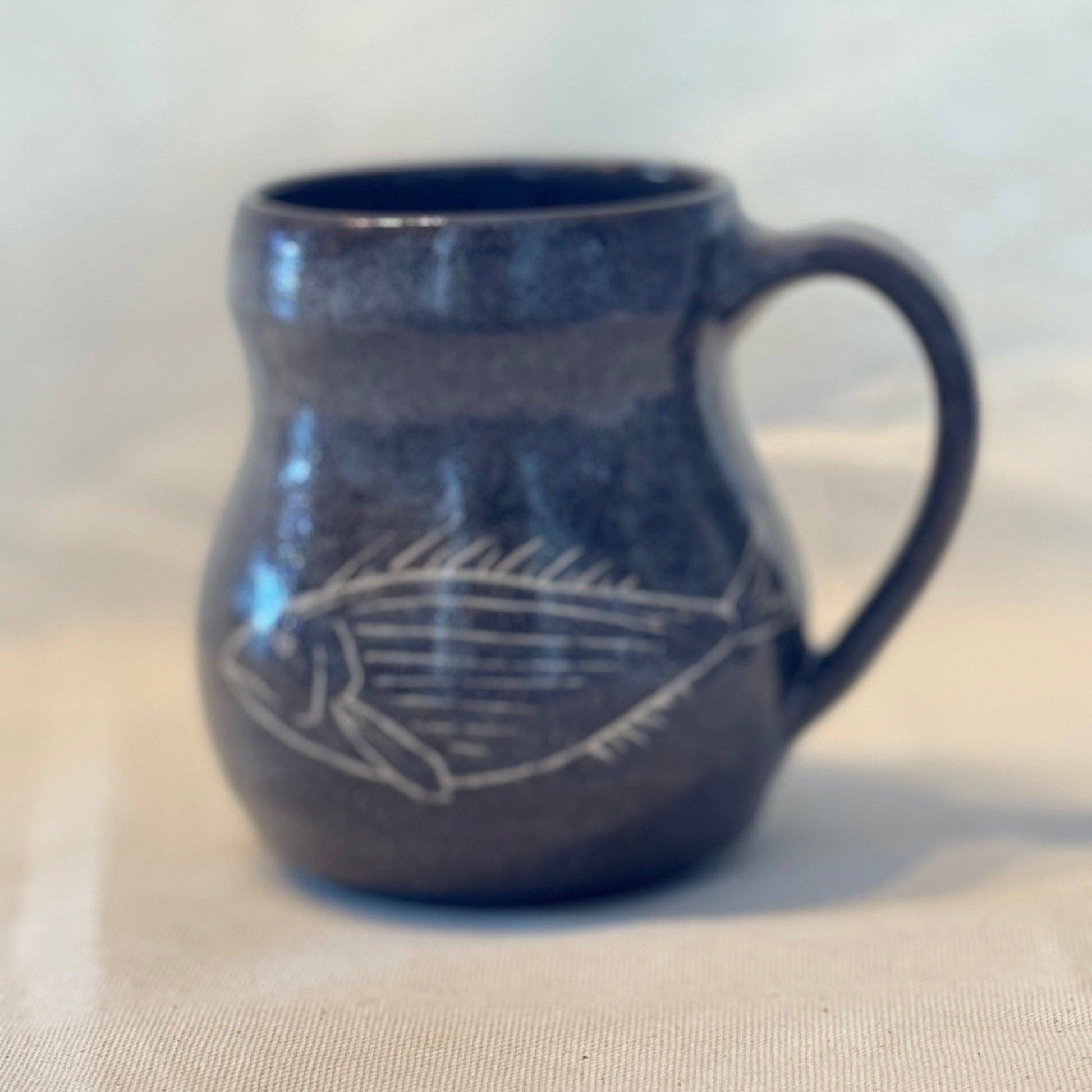Blue ceramic mug with a white fish design on a beige surface