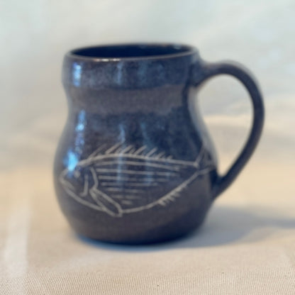 Blue ceramic mug with a white fish design on a beige surface