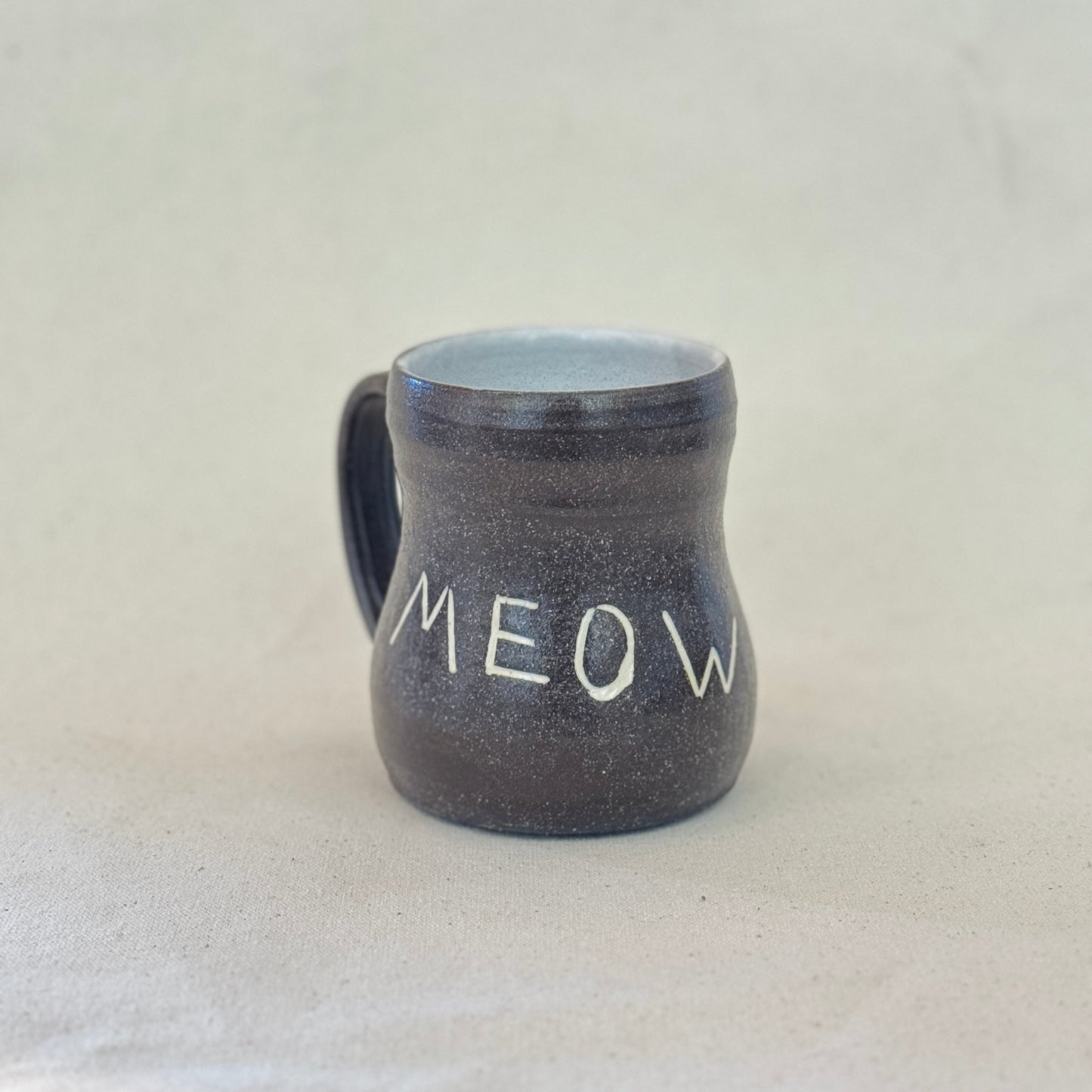 Black ceramic mug with 'MEOW' text on a light gray background