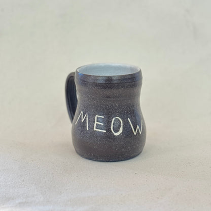 Black ceramic mug with 'MEOW' text on a light gray background