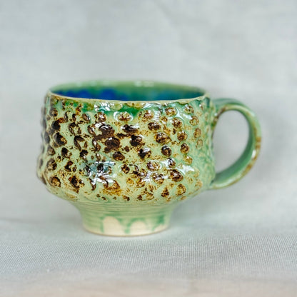 Green ceramic mug with brown speckles on a light gray background