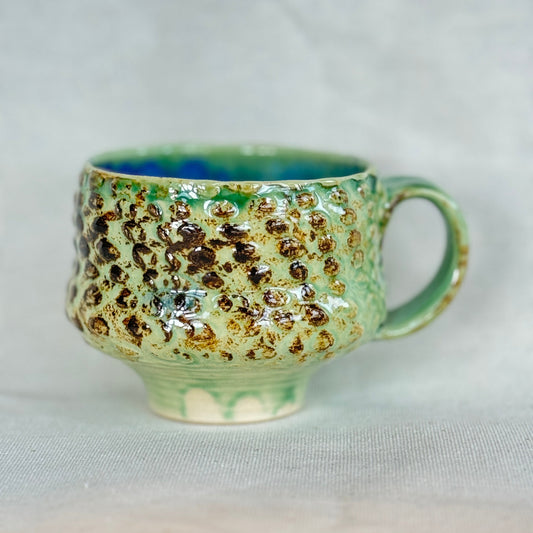 Green ceramic mug with brown speckles on a light gray background