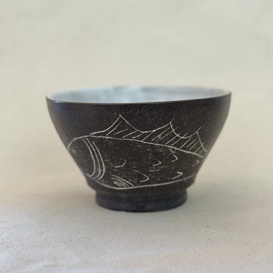Black ceramic bowl with white fish design on a light beige background