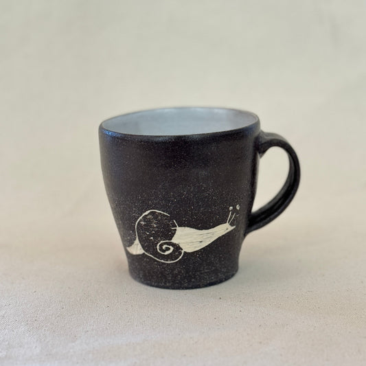 Black mug with a white snail design on a light gray background
