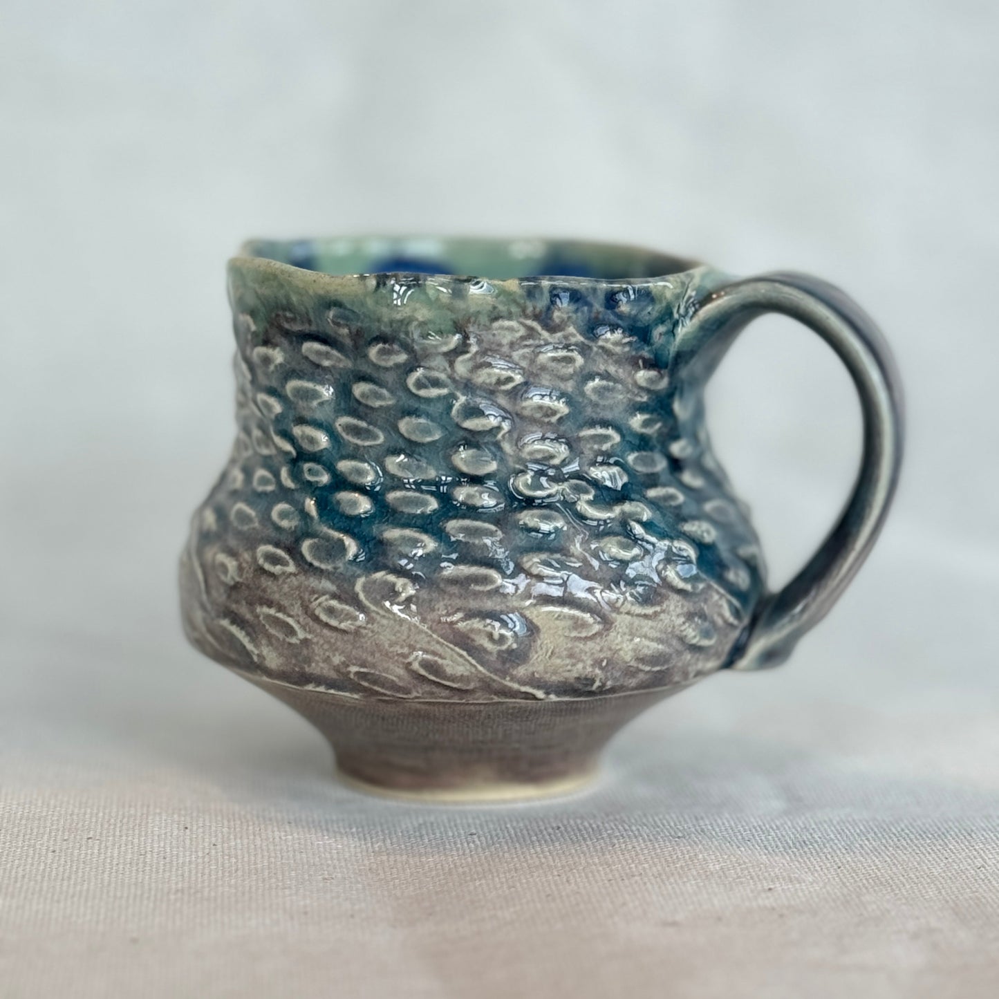 Handmade ceramic mug with textured surface on a light background