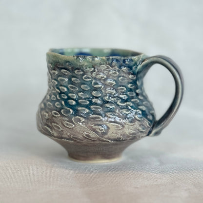 Handmade ceramic mug with textured surface on a light background