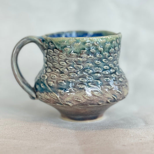 Handmade ceramic mug with textured surface on a light fabric background