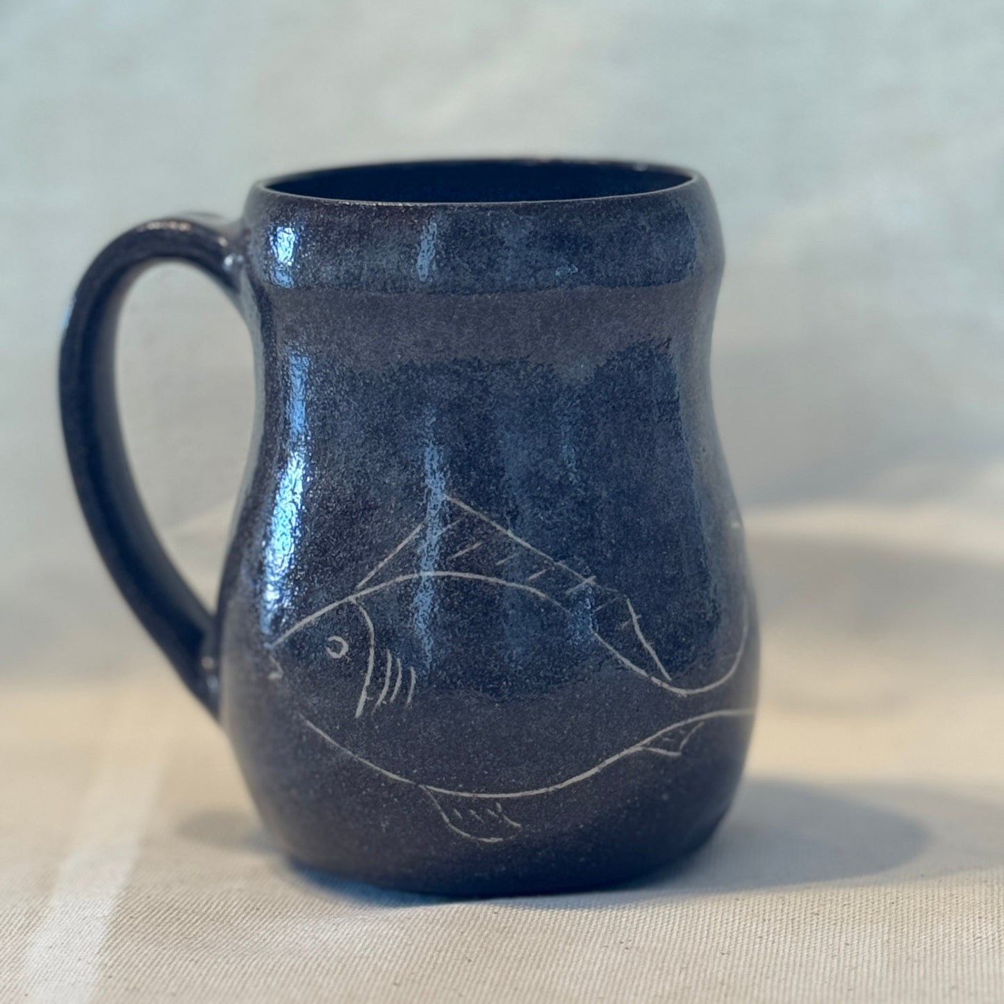 Blue ceramic mug with fish design on a beige surface