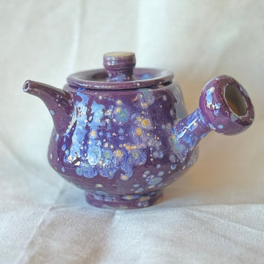 Purple ceramic teapot with speckled design on a white fabric background