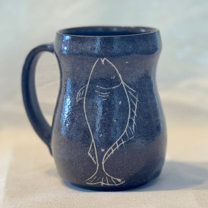 Blue ceramic mug with fish design on a beige surface