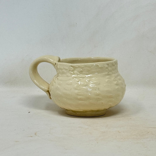 Cream-colored ceramic cup with textured surface on a white background