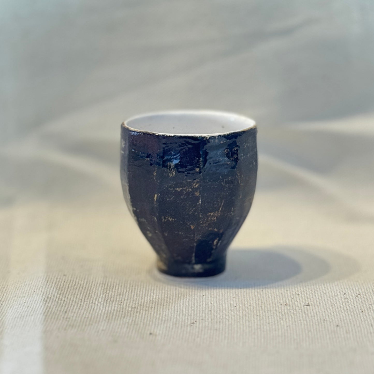 Small dark blue ceramic cup on a light fabric background