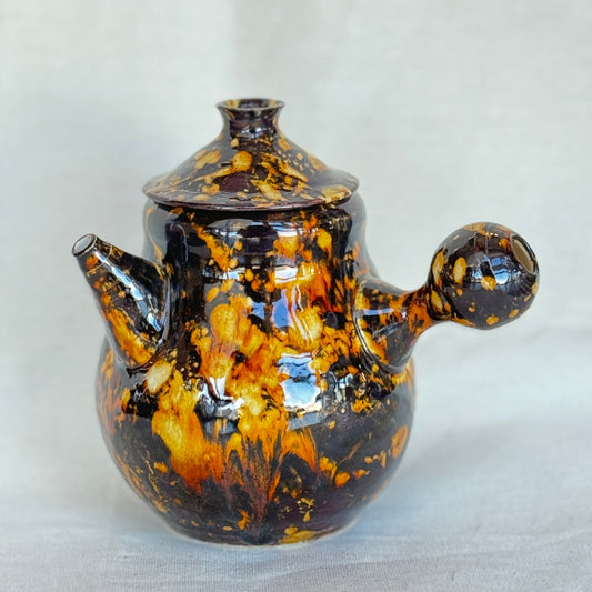 Ceramic teapot with black and orange glaze on a white background