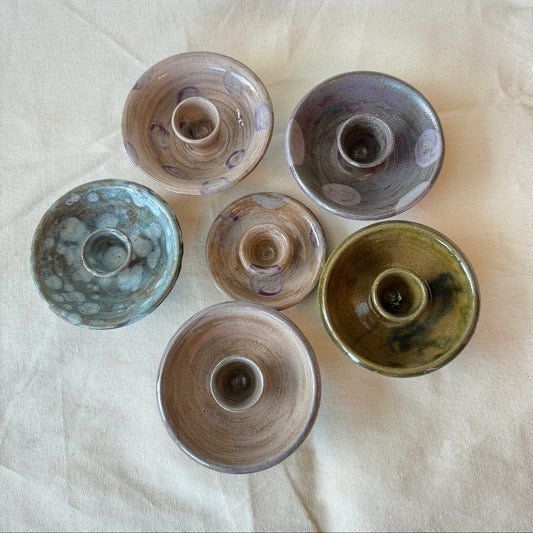 Five ceramic candle holders of different sizes and colors on a white fabric background