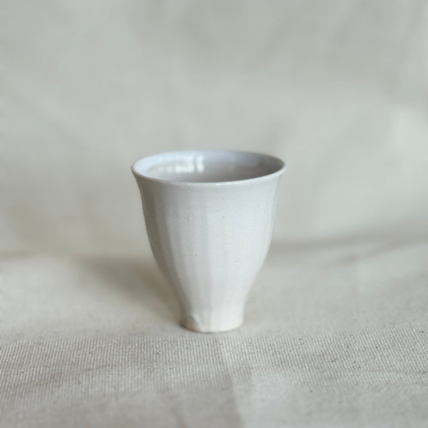 White ceramic cup on a textured beige surface with a light gray background