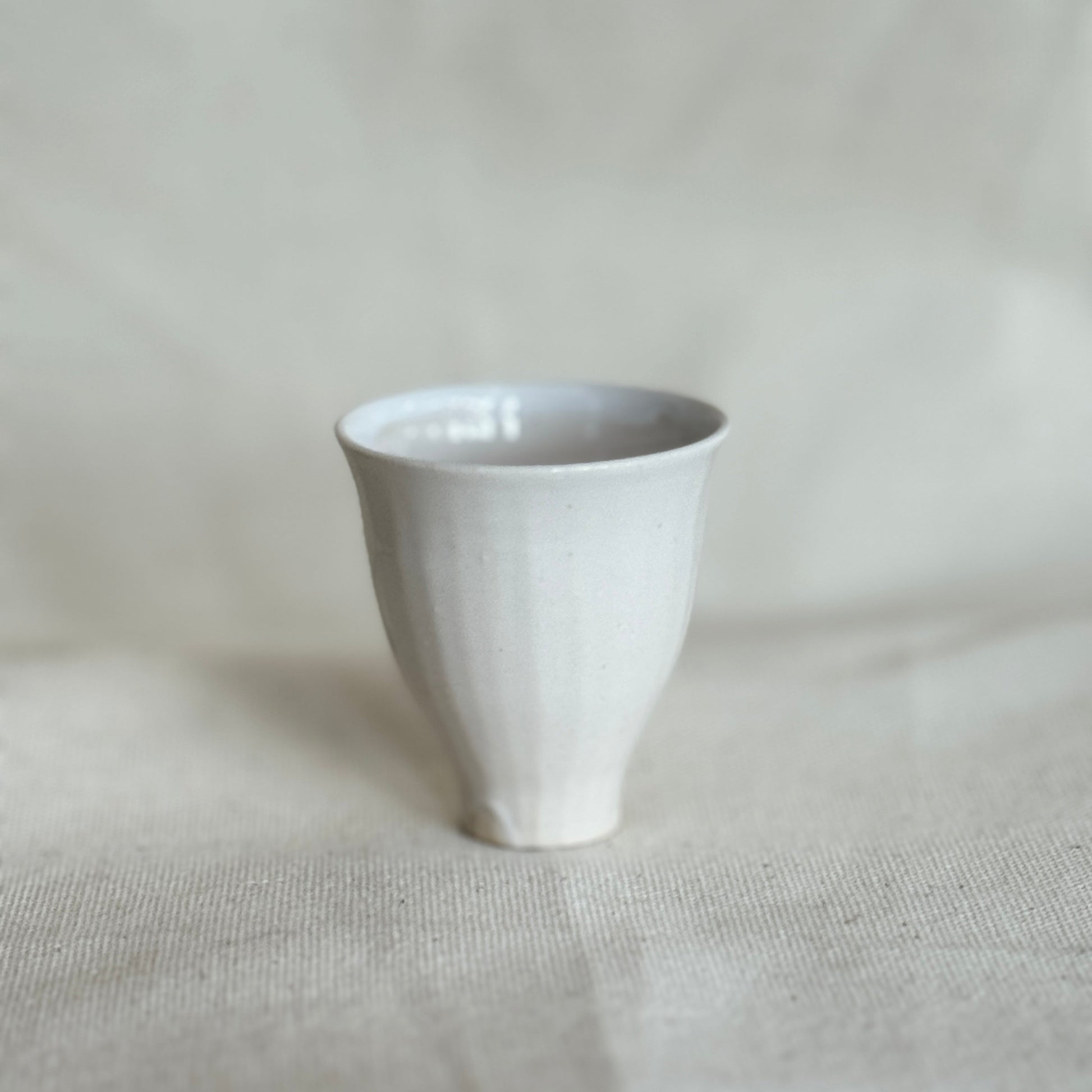 White ceramic cup on a textured beige surface with a light gray background
