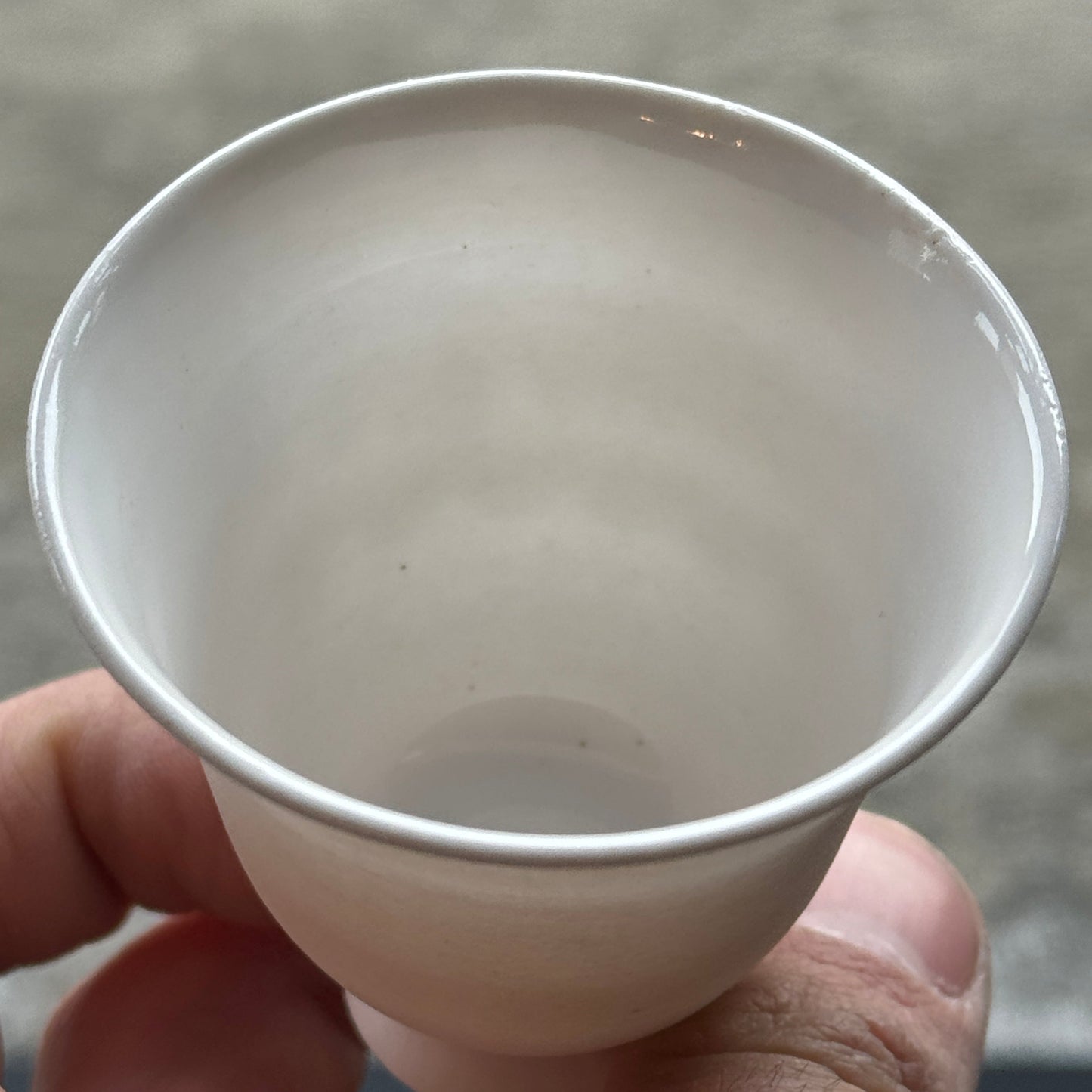 Hand holding a small white ceramic cup against a neutral background