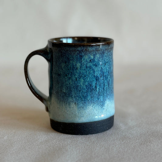Blue ceramic mug with black rim on a light gray background